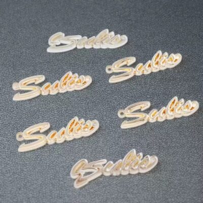 Custom 3D electroplated metal label with laser engraving attached to a fashion handbag