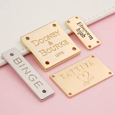 Custom laser engraved metal tag attached to clothing and bags, showing clear personalized branding