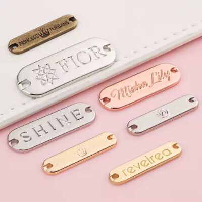 Custom laser engraved metal tag attached to clothing and bags, showing clear personalized branding
