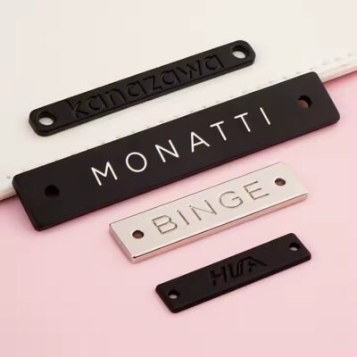 Custom laser engraved metal tag attached to clothing and bags, showing clear personalized branding